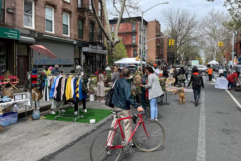 Man with red bicycle walks bike down 'open street' with vendor booths in New York City.